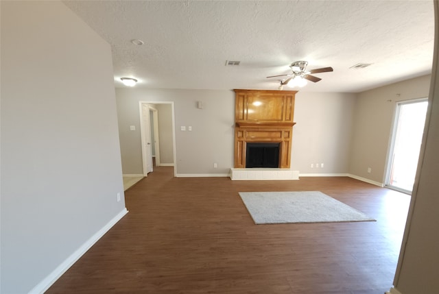 unfurnished living room featuring ceiling fan, a textured ceiling, dark hardwood / wood-style floors, and a fireplace