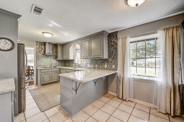 kitchen with sink, wall chimney exhaust hood, kitchen peninsula, a breakfast bar area, and gray cabinetry