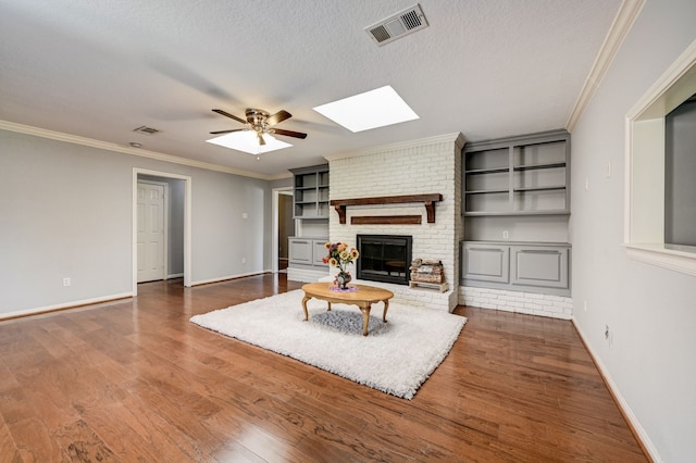 living room with a textured ceiling, ceiling fan, ornamental molding, a brick fireplace, and a skylight