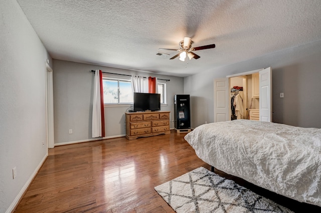 bedroom featuring hardwood / wood-style flooring, a textured ceiling, a spacious closet, a closet, and ceiling fan