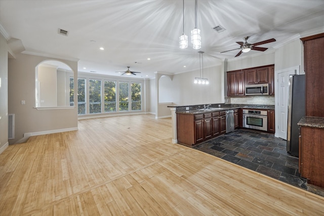 kitchen featuring wood-type flooring, kitchen peninsula, stainless steel appliances, decorative light fixtures, and crown molding