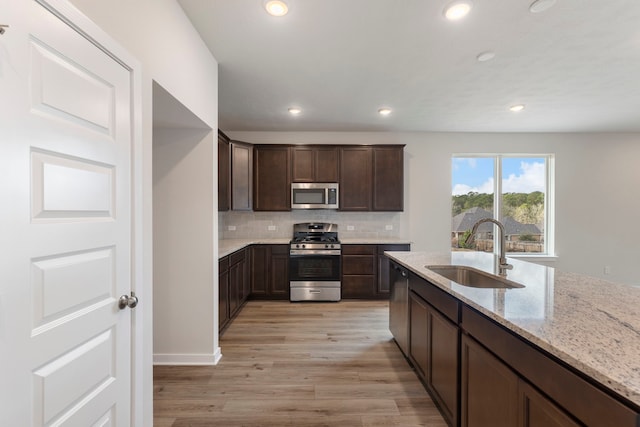 kitchen featuring sink, appliances with stainless steel finishes, backsplash, dark brown cabinetry, and light stone countertops