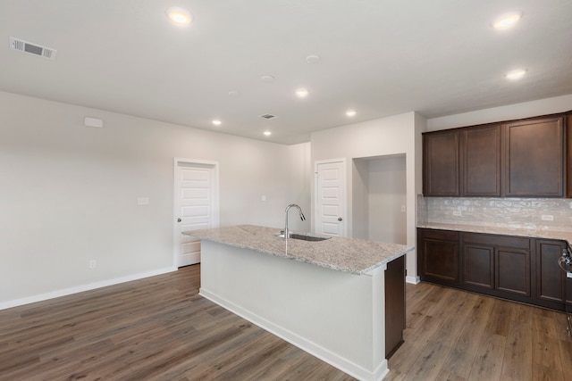 kitchen with dark hardwood / wood-style floors, an island with sink, sink, and light stone counters