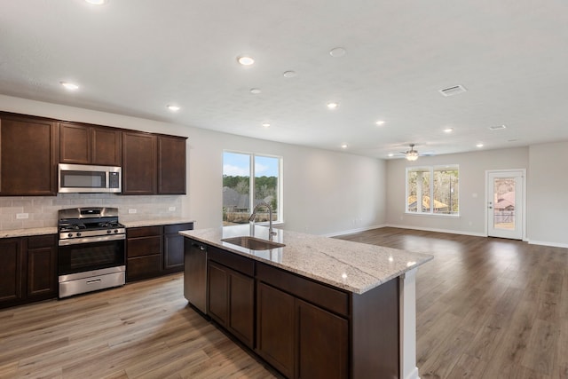 kitchen with sink, stainless steel appliances, dark brown cabinetry, decorative backsplash, and light wood-type flooring