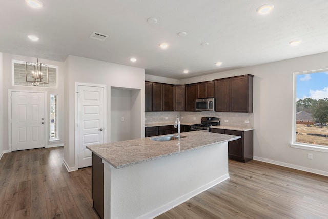 kitchen with sink, appliances with stainless steel finishes, light stone counters, tasteful backsplash, and dark brown cabinetry