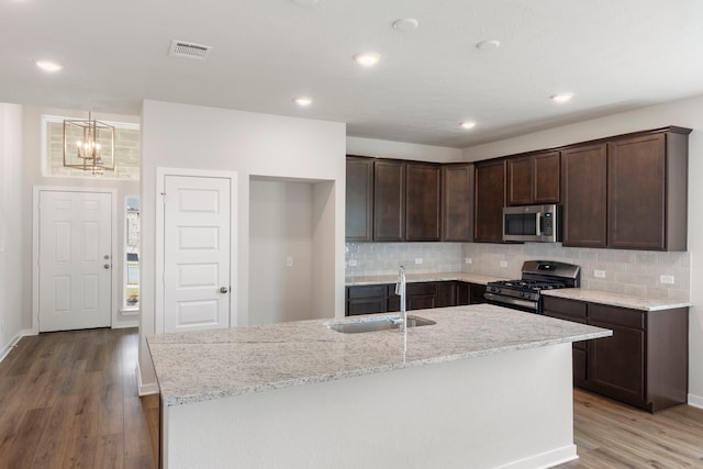 kitchen with sink, light stone counters, light wood-type flooring, range with gas stovetop, and a kitchen island with sink