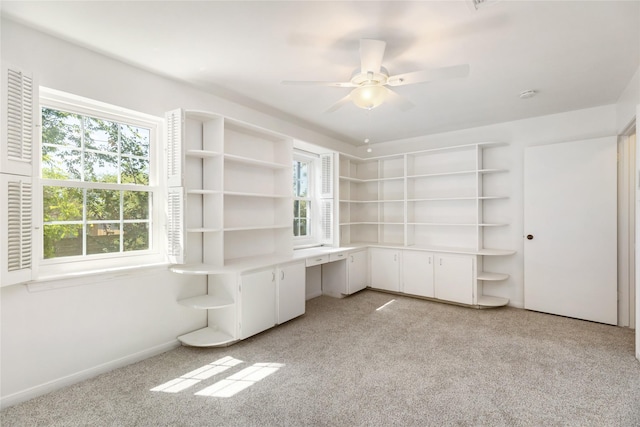 unfurnished office with light carpet, built in desk, plenty of natural light, and ceiling fan