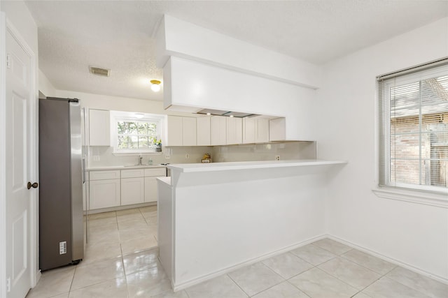 kitchen with light tile patterned floors, stainless steel refrigerator, white cabinetry, a textured ceiling, and kitchen peninsula