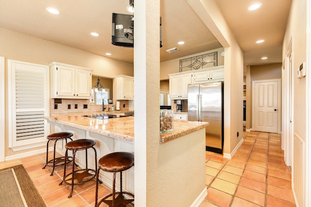 kitchen featuring decorative backsplash, stainless steel fridge, a breakfast bar area, pendant lighting, and light stone counters