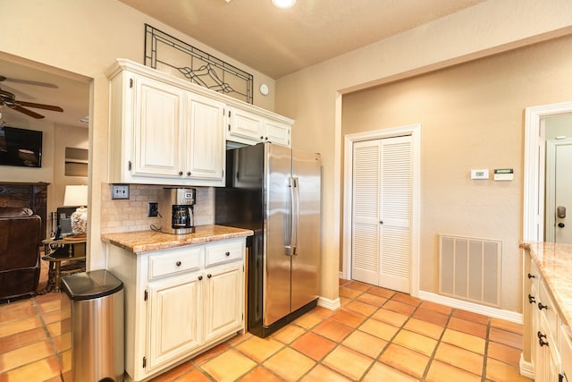 kitchen with stainless steel fridge, decorative backsplash, ceiling fan, light tile patterned flooring, and light stone counters