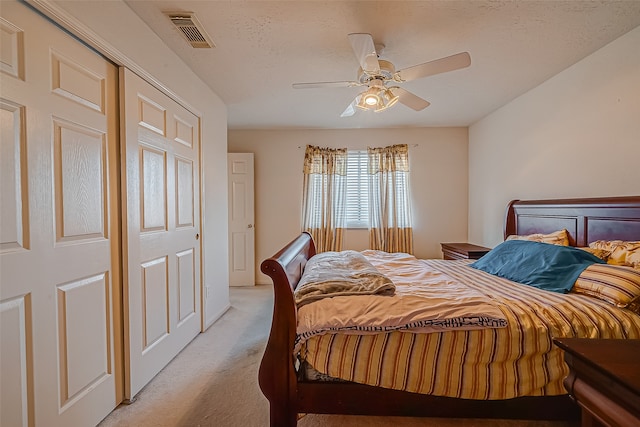 bedroom with ceiling fan, a textured ceiling, a closet, and light carpet