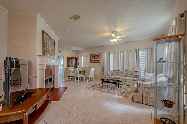 living room featuring ceiling fan, a textured ceiling, a tiled fireplace, and a wealth of natural light