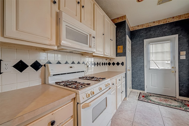 kitchen with a textured ceiling, backsplash, white appliances, and light tile patterned floors