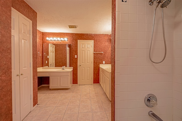 bathroom with a textured ceiling, a tile shower, tile patterned flooring, and vanity