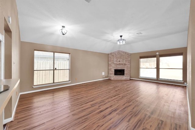 unfurnished living room featuring a wealth of natural light, vaulted ceiling, hardwood / wood-style floors, and a stone fireplace