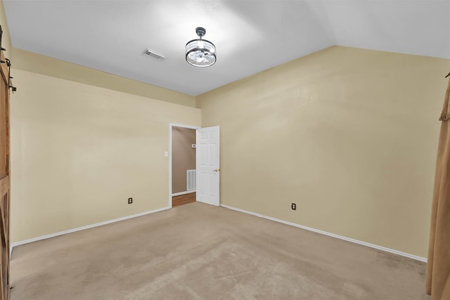 carpeted spare room with lofted ceiling and a barn door