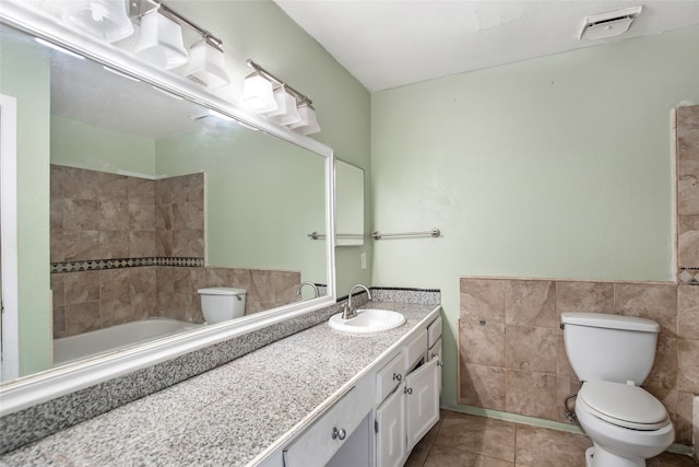 bathroom featuring tile walls, vanity, a bathing tub, tile patterned flooring, and toilet