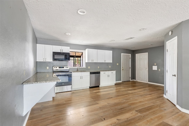 kitchen featuring light stone counters, light hardwood / wood-style floors, a textured ceiling, white cabinets, and appliances with stainless steel finishes