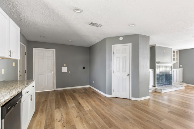 kitchen featuring white cabinets, light stone counters, light wood-type flooring, and stainless steel dishwasher