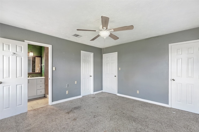 unfurnished bedroom featuring a textured ceiling, ensuite bath, ceiling fan, and light colored carpet