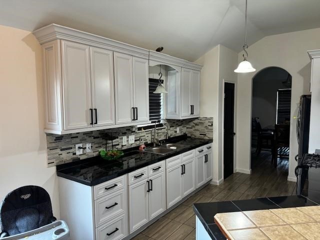 kitchen featuring sink, white cabinets, lofted ceiling, backsplash, and decorative light fixtures