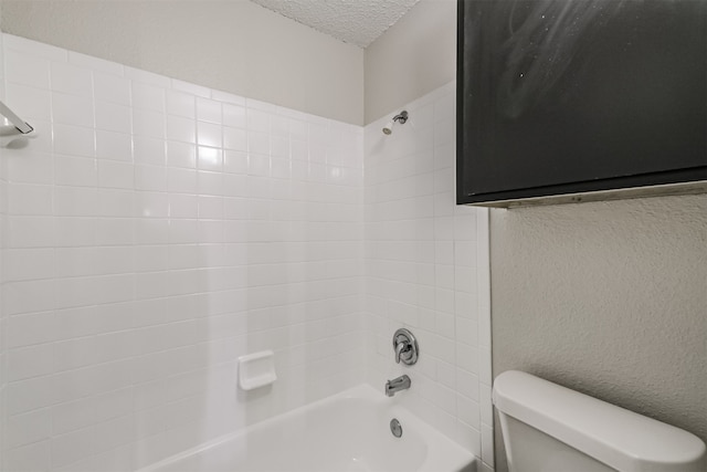 bathroom with a textured ceiling, toilet, and tiled shower / bath