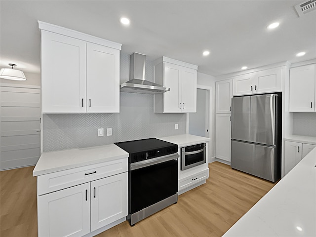 kitchen featuring wall chimney exhaust hood, stainless steel appliances, white cabinets, and light hardwood / wood-style flooring