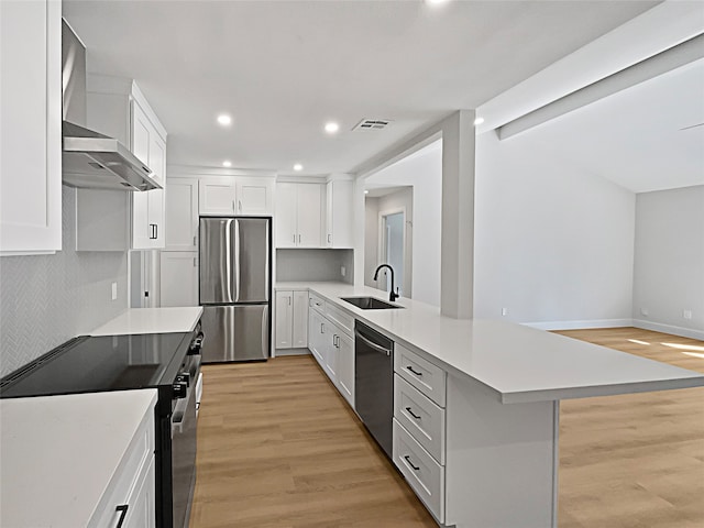 kitchen featuring light wood-type flooring, white cabinetry, appliances with stainless steel finishes, and wall chimney range hood