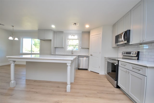 kitchen with stainless steel appliances, backsplash, a wealth of natural light, and light hardwood / wood-style floors