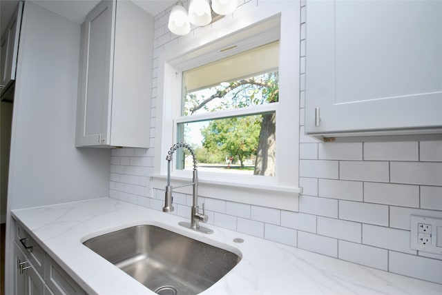 kitchen featuring backsplash, white cabinetry, light stone countertops, and sink