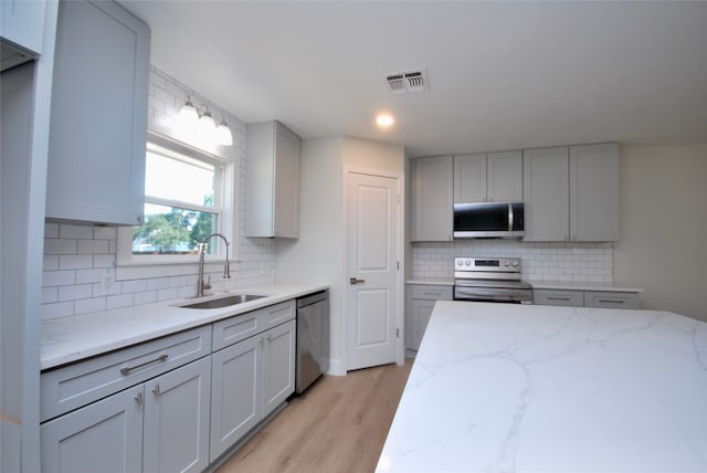 kitchen featuring gray cabinets, sink, light hardwood / wood-style flooring, stainless steel appliances, and light stone countertops