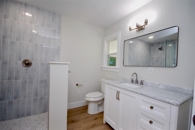 bathroom featuring toilet, tiled shower, vanity, and hardwood / wood-style floors