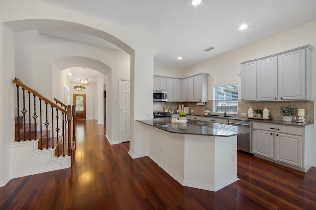 kitchen with dark stone countertops, backsplash, appliances with stainless steel finishes, and dark hardwood / wood-style floors