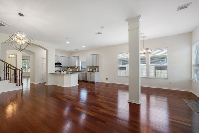 unfurnished living room featuring decorative columns, dark wood-type flooring, and a healthy amount of sunlight