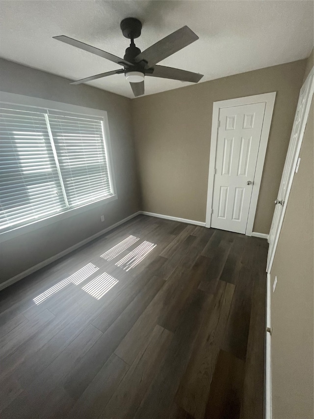 empty room featuring ceiling fan, dark wood-type flooring, and a textured ceiling