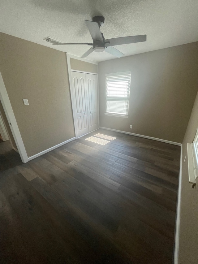 unfurnished bedroom featuring a closet, ceiling fan, dark hardwood / wood-style floors, and a textured ceiling