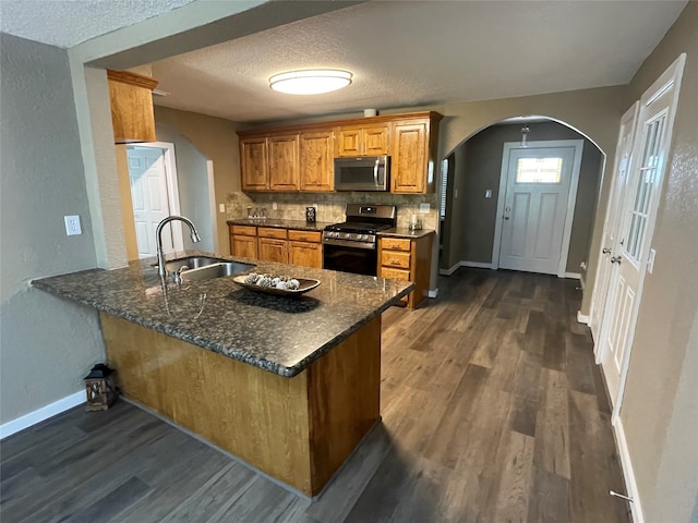 kitchen featuring dark stone counters, sink, kitchen peninsula, appliances with stainless steel finishes, and dark hardwood / wood-style flooring