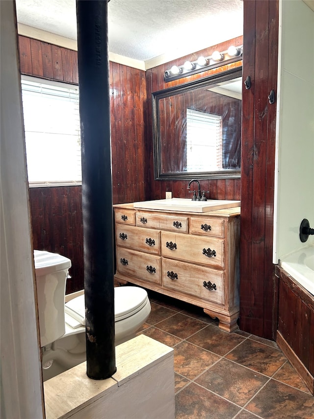 bathroom featuring a textured ceiling, a washtub, wood walls, vanity, and toilet