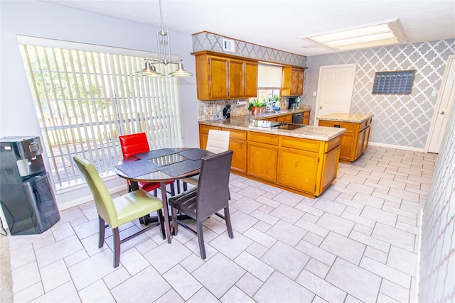 kitchen with pendant lighting, black electric stovetop, kitchen peninsula, decorative backsplash, and light stone countertops