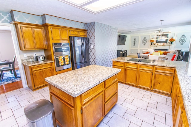 kitchen with hanging light fixtures, light stone counters, a kitchen island, stainless steel appliances, and ceiling fan