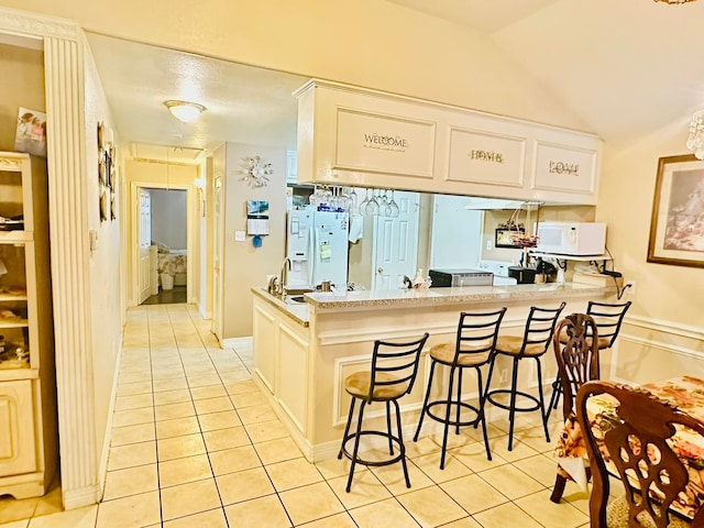 kitchen with light tile patterned flooring, a breakfast bar area, lofted ceiling, kitchen peninsula, and white appliances