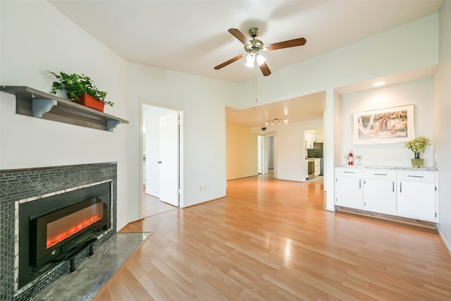 unfurnished living room featuring ceiling fan, light wood-type flooring, and a tile fireplace