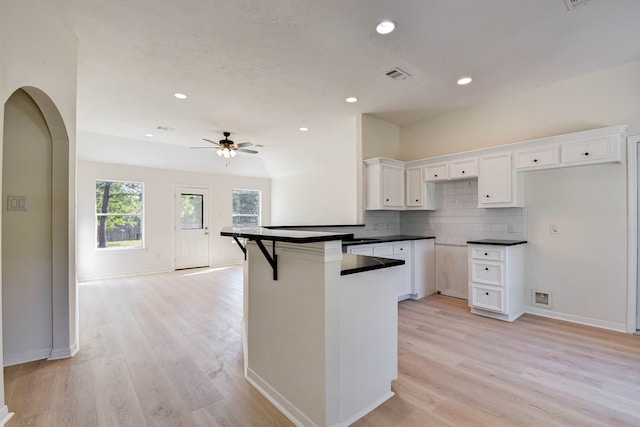 kitchen with white cabinets, a breakfast bar, ceiling fan, and light hardwood / wood-style flooring