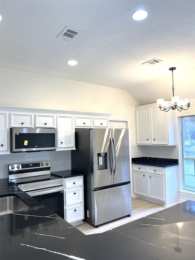 kitchen with stainless steel appliances, vaulted ceiling, decorative light fixtures, an inviting chandelier, and white cabinetry