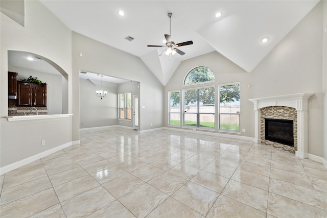 unfurnished living room featuring high vaulted ceiling, ceiling fan with notable chandelier, light tile patterned floors, and a stone fireplace