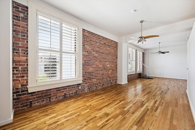 unfurnished living room with light hardwood / wood-style floors, brick wall, and ceiling fan