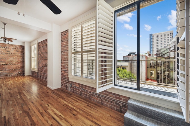 unfurnished room with a healthy amount of sunlight, ceiling fan, wood-type flooring, and brick wall