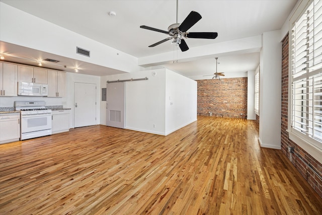 unfurnished living room with a barn door, light hardwood / wood-style floors, ceiling fan, and brick wall