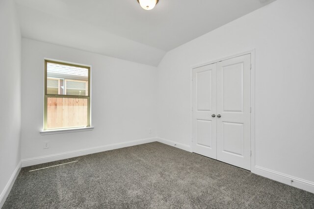 unfurnished room with dark colored carpet and vaulted ceiling