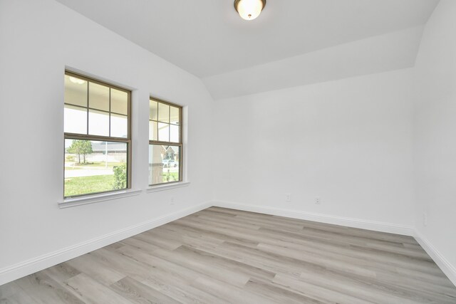 spare room featuring light wood-type flooring and vaulted ceiling